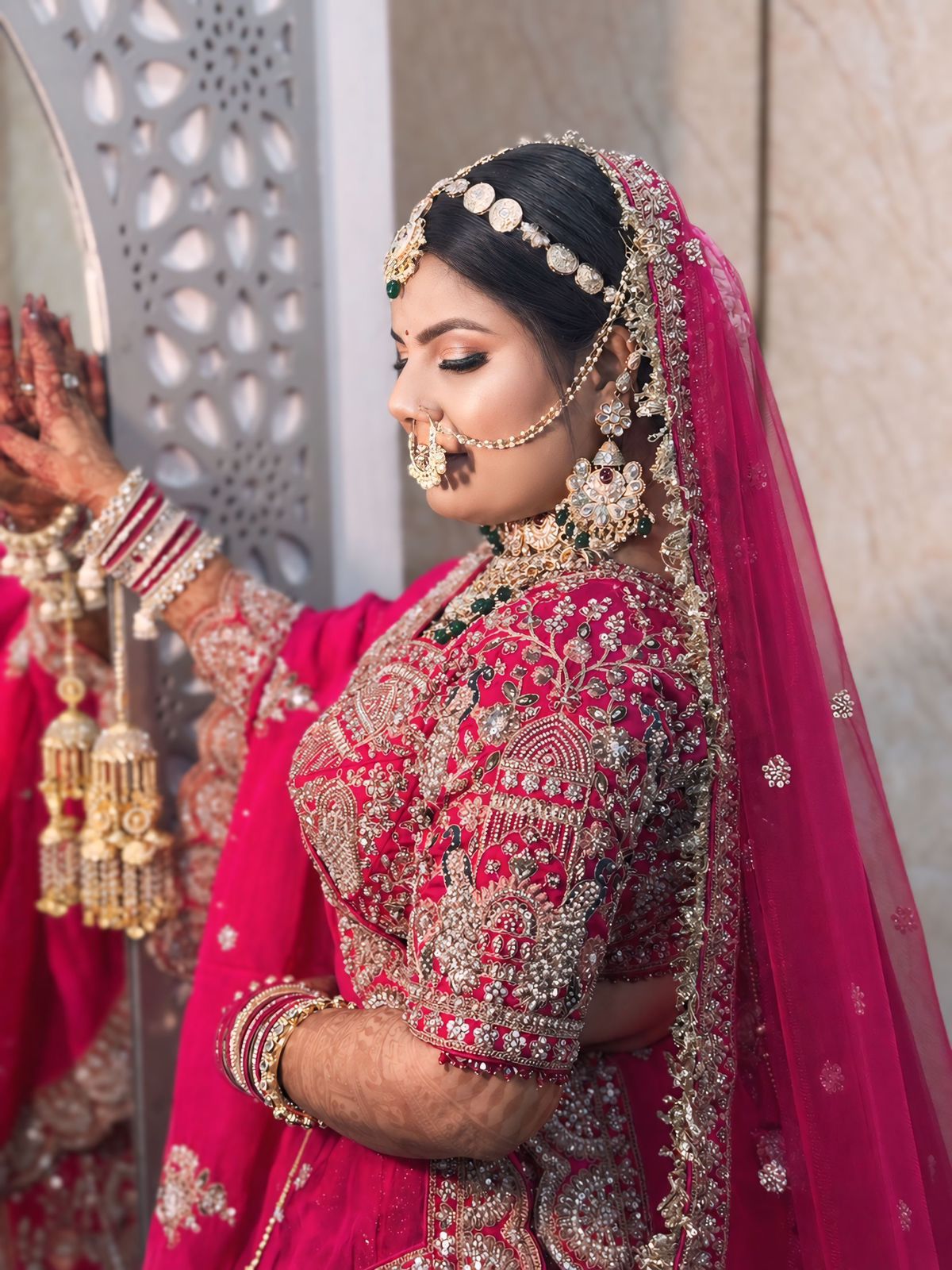 Bride in hot-pink lehenga at mirror — side profile